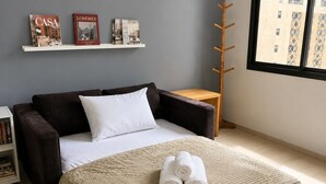 Ein Schlafzimmer mit einem Bett, einem Nachttisch, einem Holz-Kleiderständer und einem Fenster mit Blick auf Gebäude.