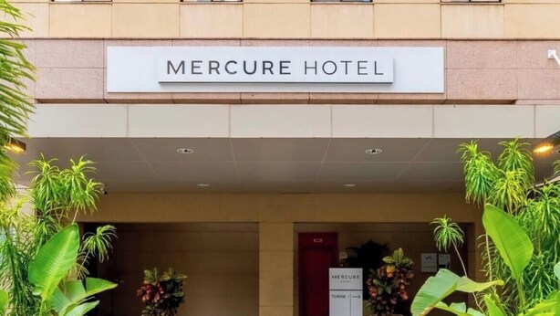 Der Eingang zum Mercure Hotel mit einem Schild über der Tür, Blumentöpfen und einem Fliesenboden.