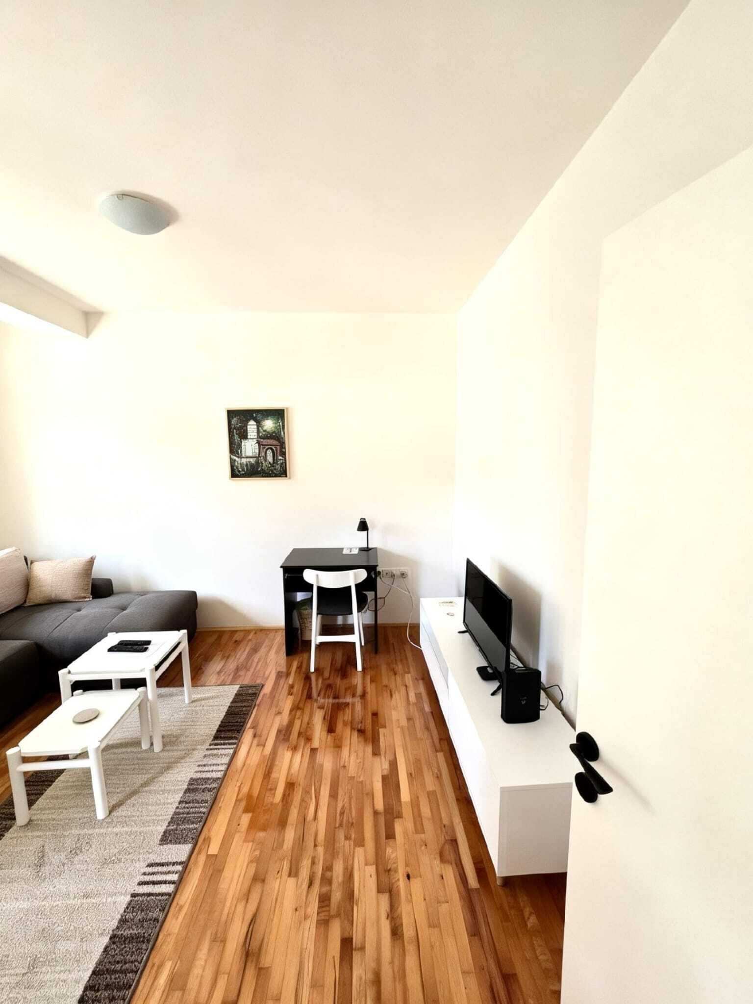 A modern living room with a sofa, a small table, a TV, and a desk with a chair.