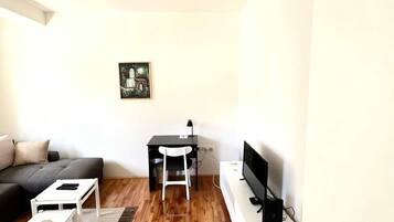 A modern living room with a sofa, a small table, a TV, and a desk with a chair.