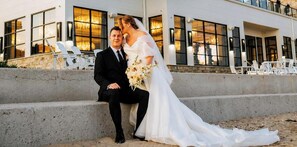 Un couple est assis sur des marches en béton devant un immeuble doté de grandes fenêtres et d’une terrasse.