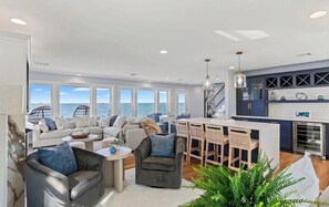 Un vaste espace de vie avec vue sur la mer, une cuisine dotée de meubles sombres et un coin repas avec des chaises en bois.
