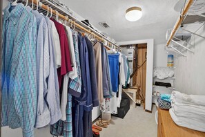 A walk-in closet with hanging clothes, a suitcase, and a bed with a white blanket. - Beautiful 4-bedroom beach front house in Ponce Inlet (Port Orange)