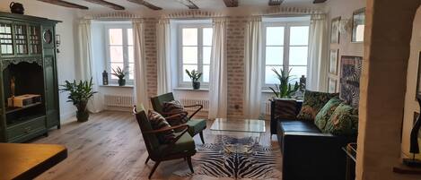 A cozy living room with a wooden floor, green armchairs, a glass coffee table, a zebra rug, and a green cabinet.