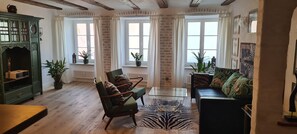Ein gemütliches Wohnzimmer mit Holzboden, grünen Sesseln, einem Glastisch, einem Zebra-Teppich und einem grünen Schrank.