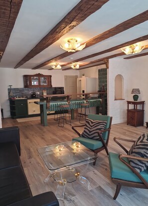 Un vaste espace de vie avec une table basse en verre, un plancher en bois et une cuisine à l’arrière-plan.