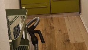 Una habitació amb un armari verd, una prateleira de fusta i un aspirador.