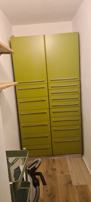 Ein Zimmer mit einem grünen Kleiderschrank, einem Holzbodenregal und einem Staubsauger.