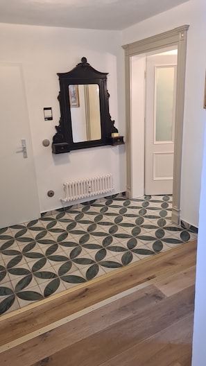 Ein Zimmer mit einem gemusterten Boden, einem Heizkörper, einer Tür und einem Spiegel.