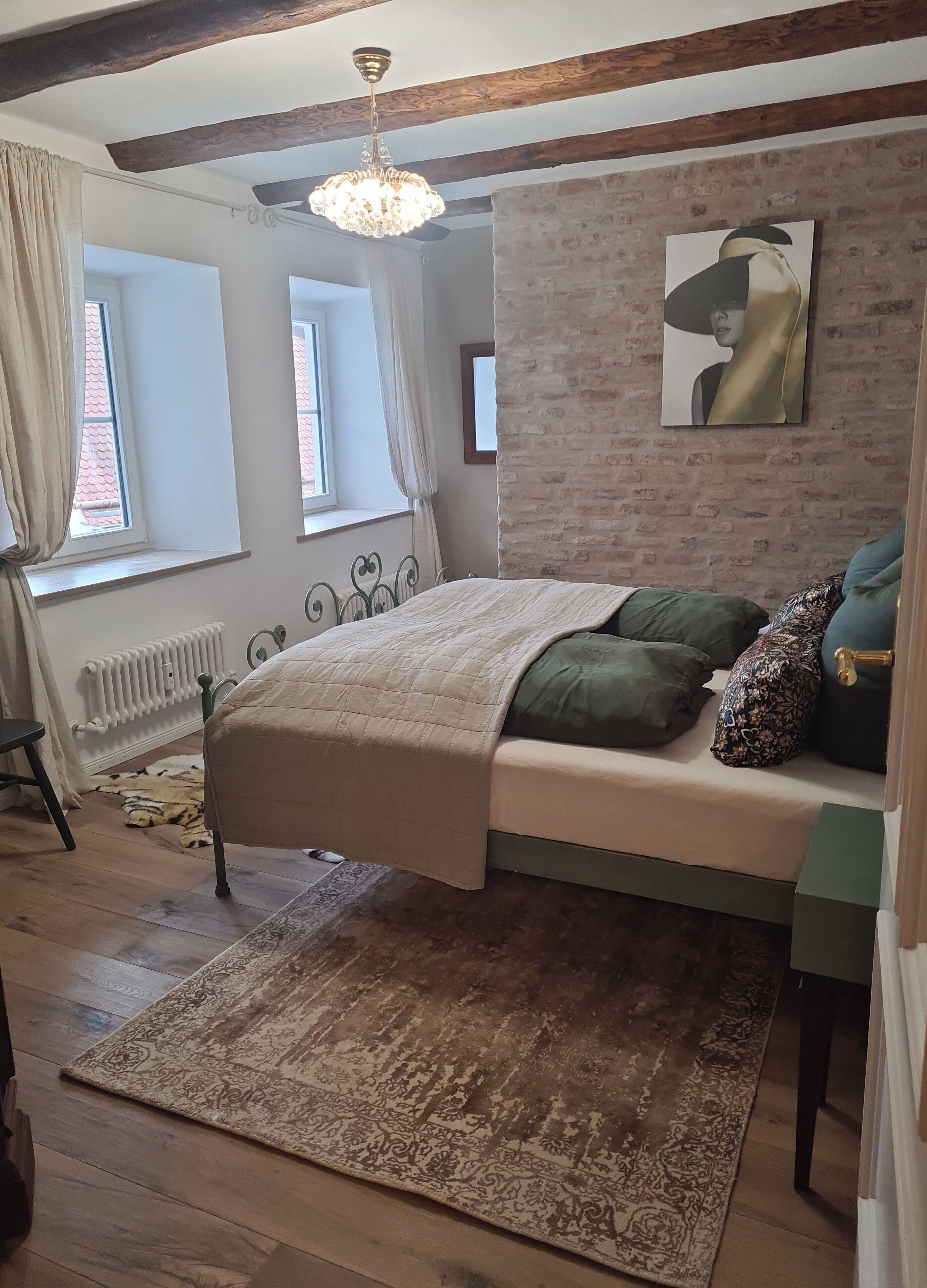 Une chambre à coucher avec un lit, un radiateur, une fenêtre, un mur en briques et un lustre.