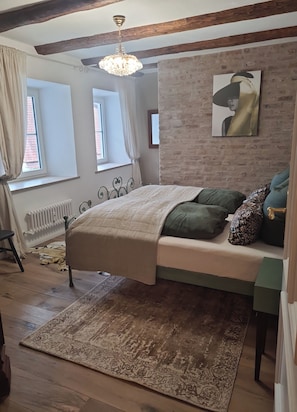 Une chambre à coucher avec un lit, un radiateur, une fenêtre, un mur en briques et un lustre.