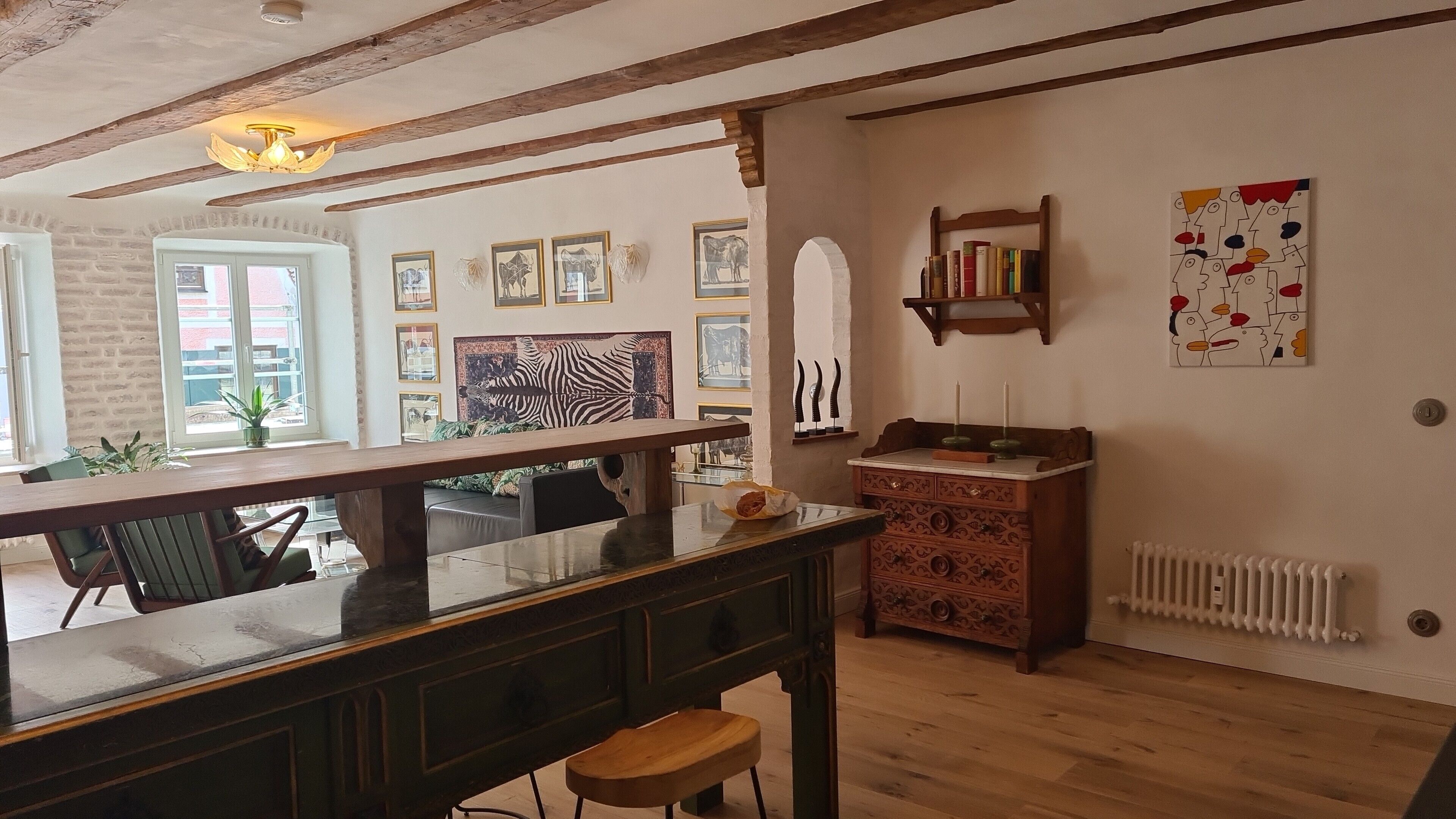 Ein Zimmer mit Holztisch, Stühlen, einer Heizung und Bildern an den Wänden.