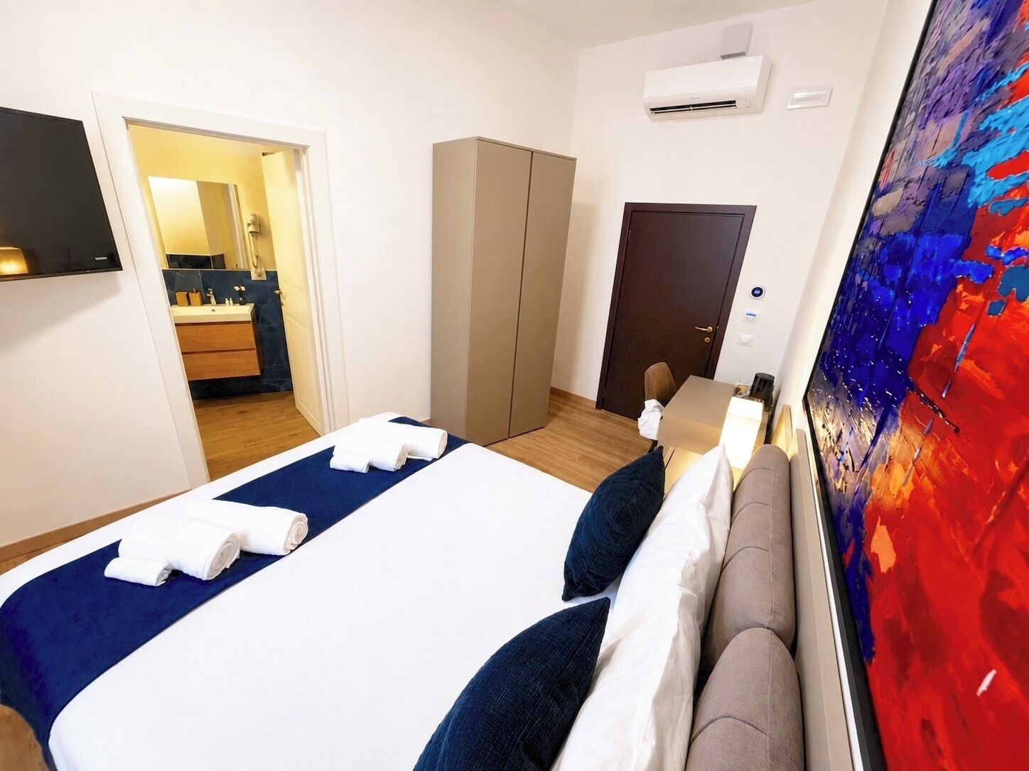 Une chambre d’hôtel avec un lit, une armoire, un appareil de climatisation et un tableau au mur.