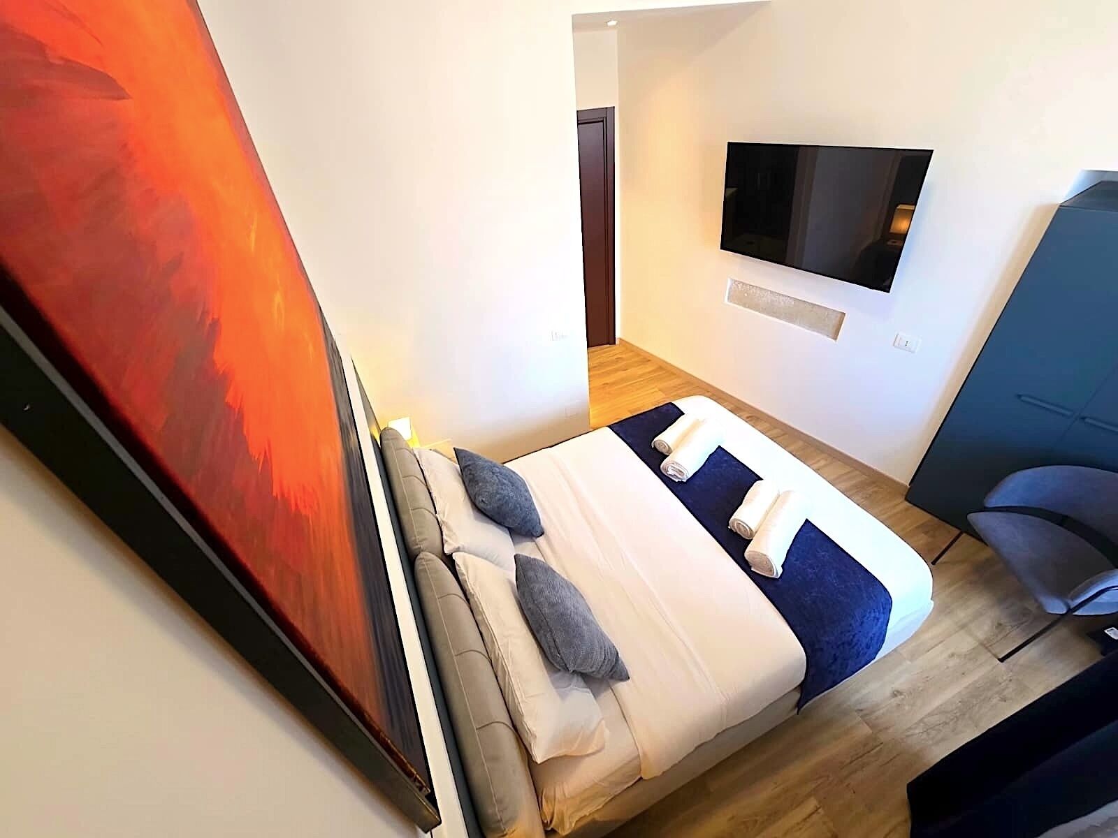 Ein modernes Hotelzimmer mit einem Bett, einem flachbildfernseher an der Wand und einem großen Gemälde.
