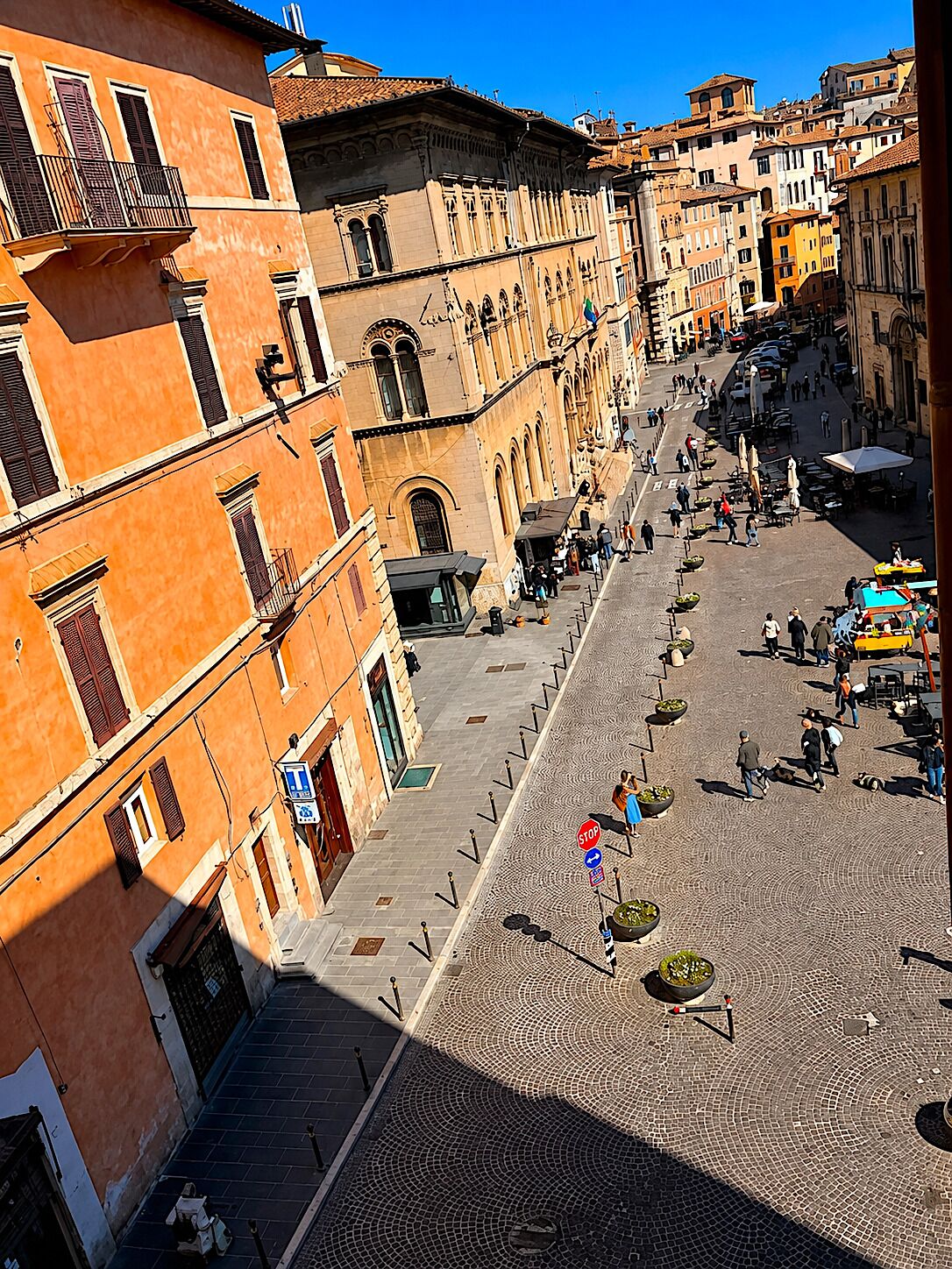 A cobblestone street with historic buildings, outdoor seating, and a clear blue sky.