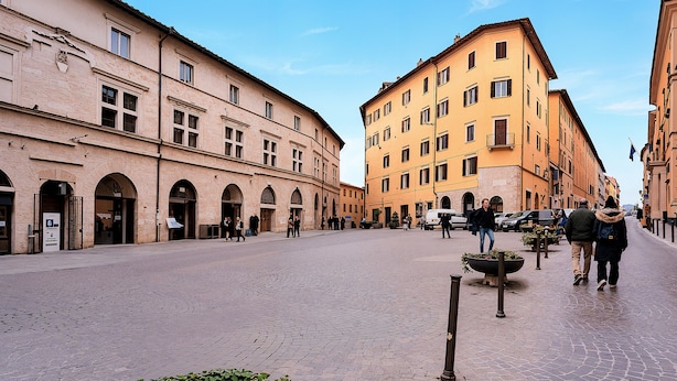 Una strada acciottolata fiancheggiata da edifici storici, alcuni con portali ad arco e altri con balconi.
