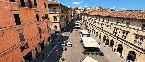 A cobblestone street lined with historic buildings, outdoor seating, and a white car parked on the street.