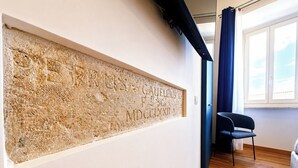 A room with a wall-mounted artwork, a window with curtains, and a wooden floor.