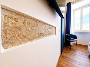 Ein Zimmer mit einem an der Wand befestigten Kunstwerk, einem mit Vorhängen versehenen Fenster und einem Holzboden.