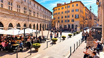 Un café animé avec une terrasse et des tables, situé en plein air et entouré de bâtiments historiques.