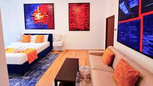 A modern hotel room with a bed, a sofa, a coffee table, and two abstract paintings on the walls.