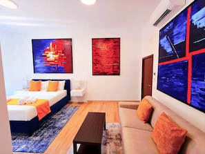 Ein modernes Hotelzimmer mit Bett, Sofa, Couchtisch und zwei abstrakten Bildern an den Wänden.