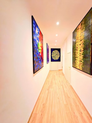 A hallway with wooden flooring and three large abstract paintings on the walls.