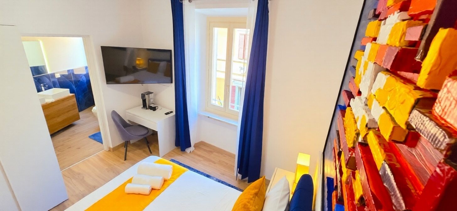 A hotel room with a bed, a desk, a chair, a TV, and a window with curtains.