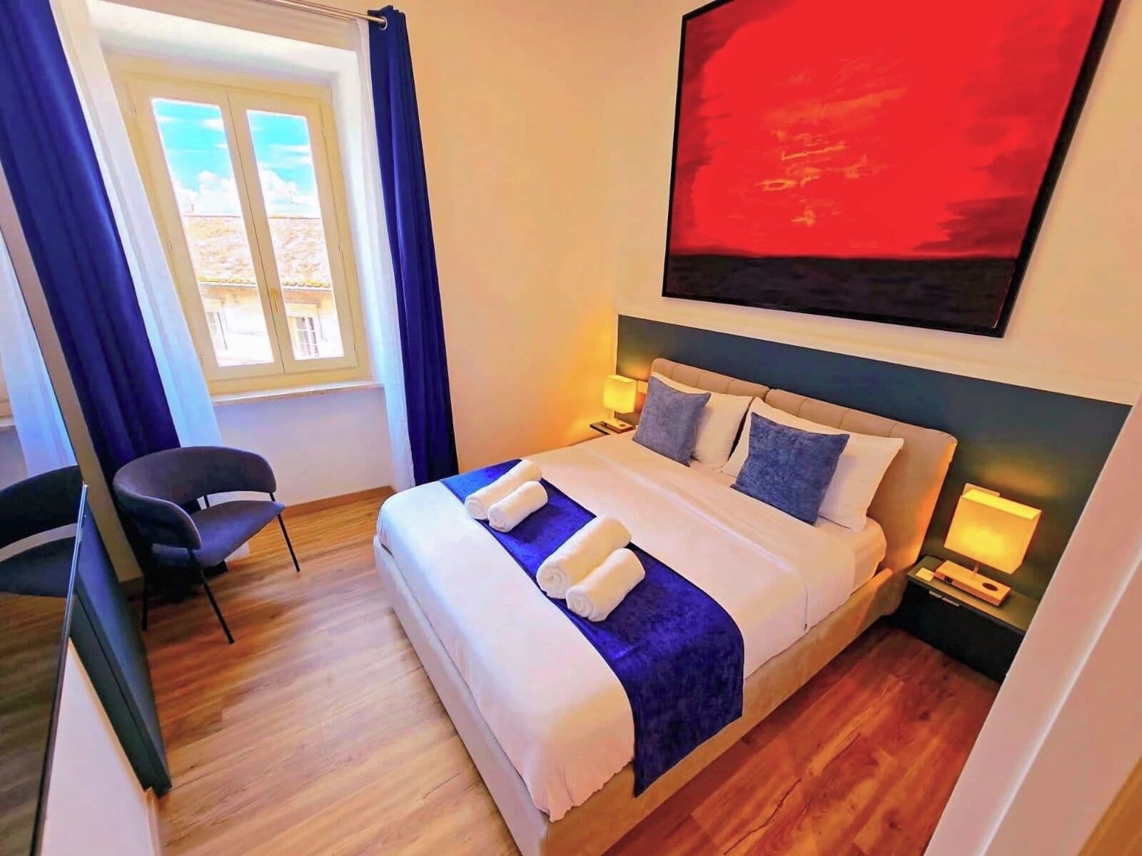 Une chambre d’hôtel avec un lit, deux tables de chevet, une chaise, une fenêtre avec des rideaux et un tableau au mur.