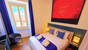 A hotel room with a bed, two bedside tables, a chair, a window with curtains, and a painting on the wall.