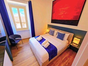 Ein Hotelzimmer mit einem Bett, zwei Nachttischen, einem Sessel, einem Fenster mit Vorhängen und einem Bild an der Wand.