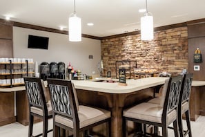 Een bar met een stenen muur, barstoelen, een koffiehoek en een televisie.