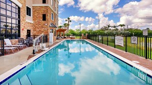 A swimming pool with lounge chairs, a covered seating area, and a brick wall. - Accessible 1BR Suite w/ Kitchen + Free Breakfast (Davie)