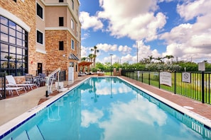 A swimming pool with lounge chairs, a covered seating area, and a brick wall. - Accessible 1BR Suite w/ Kitchen + Free Breakfast (Davie)