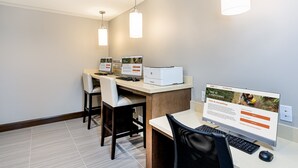 A modern office space with three desks, each with a computer and chair, and a large monitor displaying a webpage. - Accessible 1BR Suite w/ Kitchen + Free Breakfast (Davie)