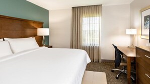 A hotel room with a large bed, a desk, a chair, a lamp, and a window with curtains. - Accessible 1BR Suite w/ Kitchen + Free Breakfast (Davie)
