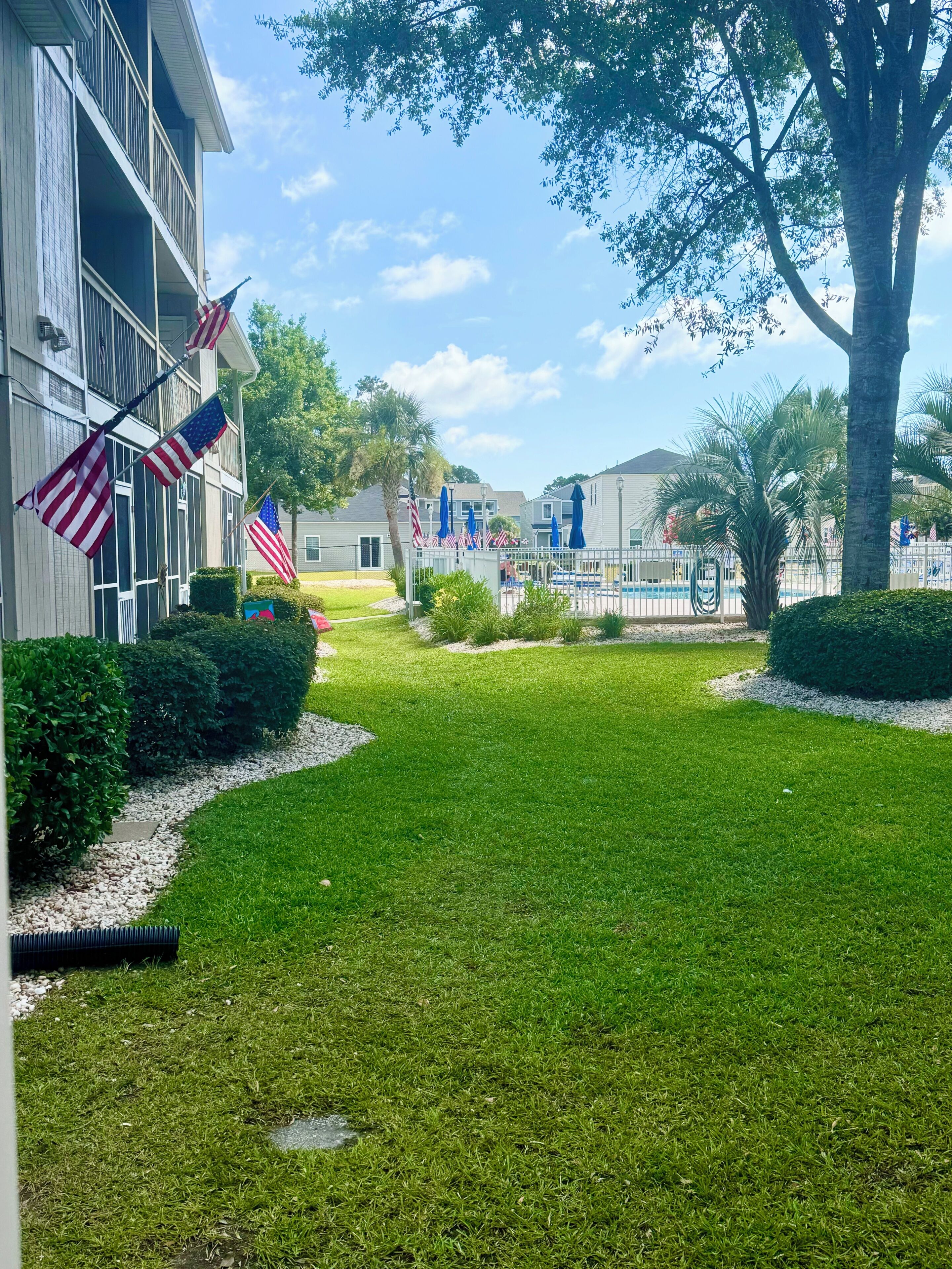 A well-maintained lawn, American flags, and a pool area with umbrellas.