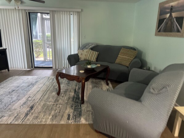 Ein Wohnzimmer mit einer Couch, einem Couchtisch und einem großen Fenster mit Jalousien.