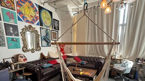 A room with a hammock chair, a brown leather sofa, a wooden coffee table, and a large mirror on the wall. - Brooklyn Loft with 8 ft pool table, king sized bed, full wall of windows and AC! (brooklyn)