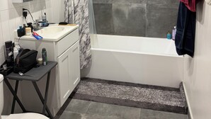A bathroom with a bathtub, toilet, vanity, and a shower area. - Brooklyn Loft with 8 ft pool table, king sized bed, full wall of windows and AC! (brooklyn)