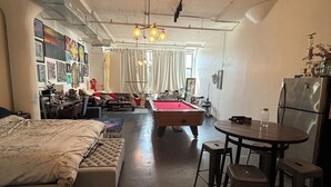 A room with a bed, a pool table, a dining table with chairs, and a refrigerator. - Brooklyn Loft with 8 ft pool table, king sized bed, full wall of windows and AC! (brooklyn)