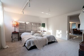 A bedroom with a large bed, bedside tables, a lamp, and a view of another room.