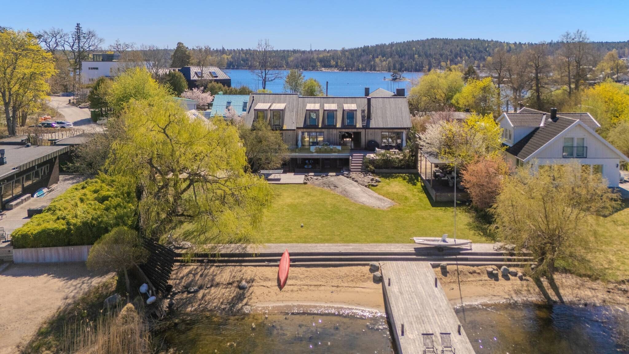Una casa moderna con un'ampia terrazza che si affaccia su un fiume, circondata da alberi e una vista limpida su un lago.