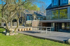 A modern house with a wooden deck, outdoor seating, and a stone wall.