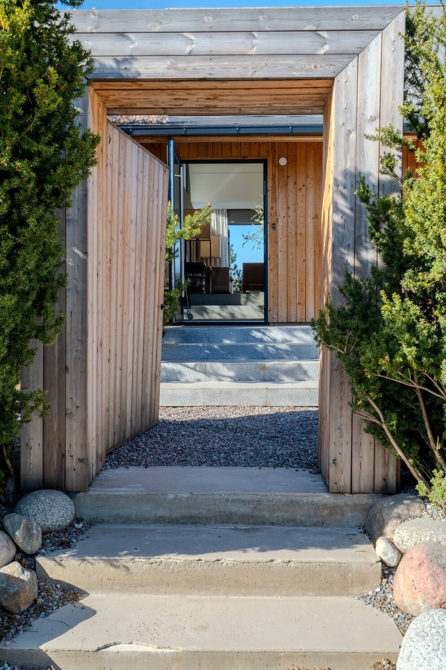 A wooden entrance with steps leading to a modern building, surrounded by rocks and greenery.