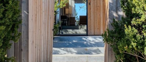 A wooden entrance with steps leading to a modern building, surrounded by rocks and greenery.