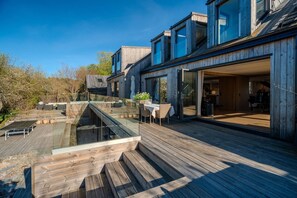 A modern house with a wooden deck, a glass-enclosed outdoor area, and a dining setup.