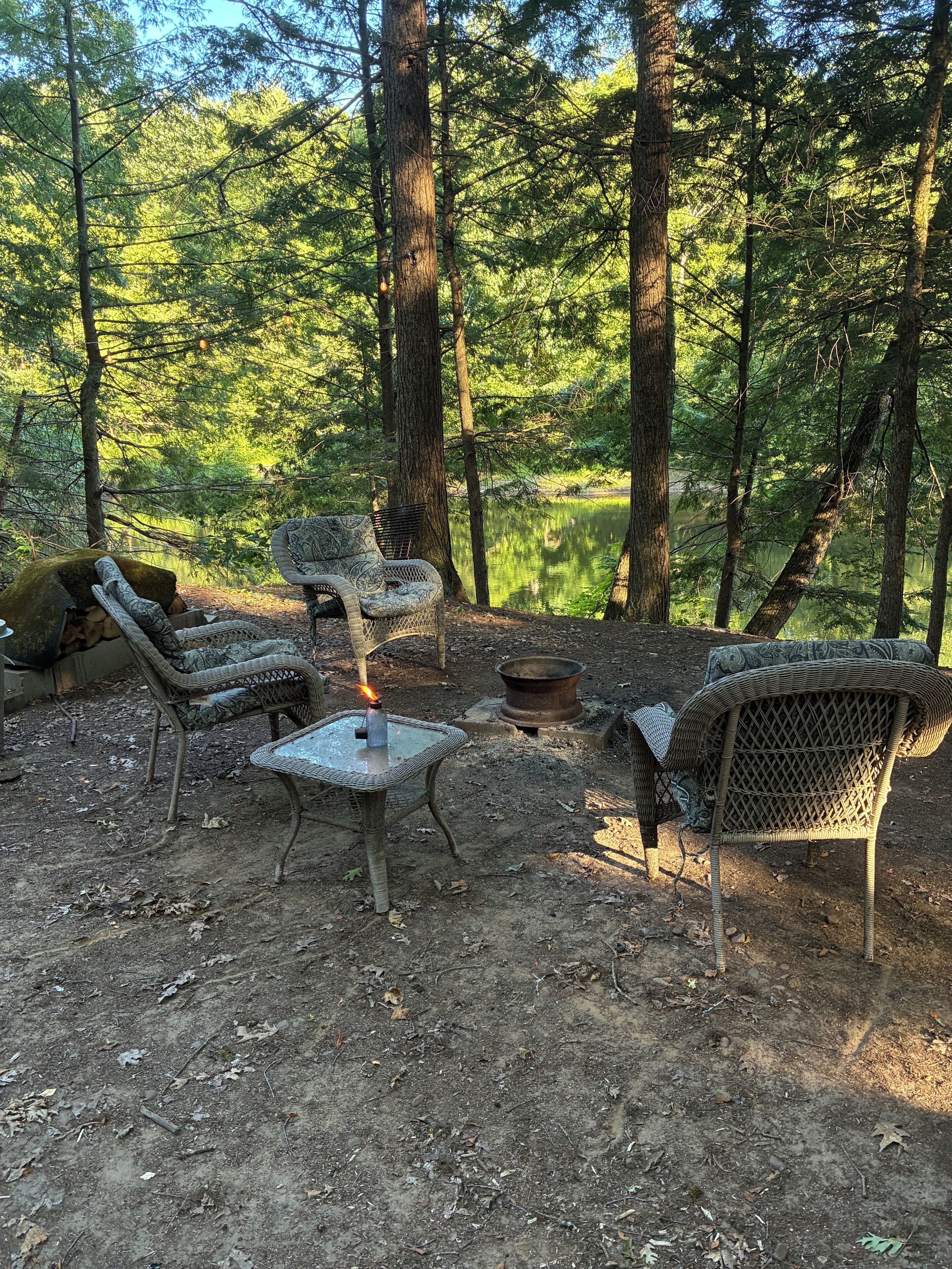 En skovcampingplads med fletmøbler, bålsted og et bord.