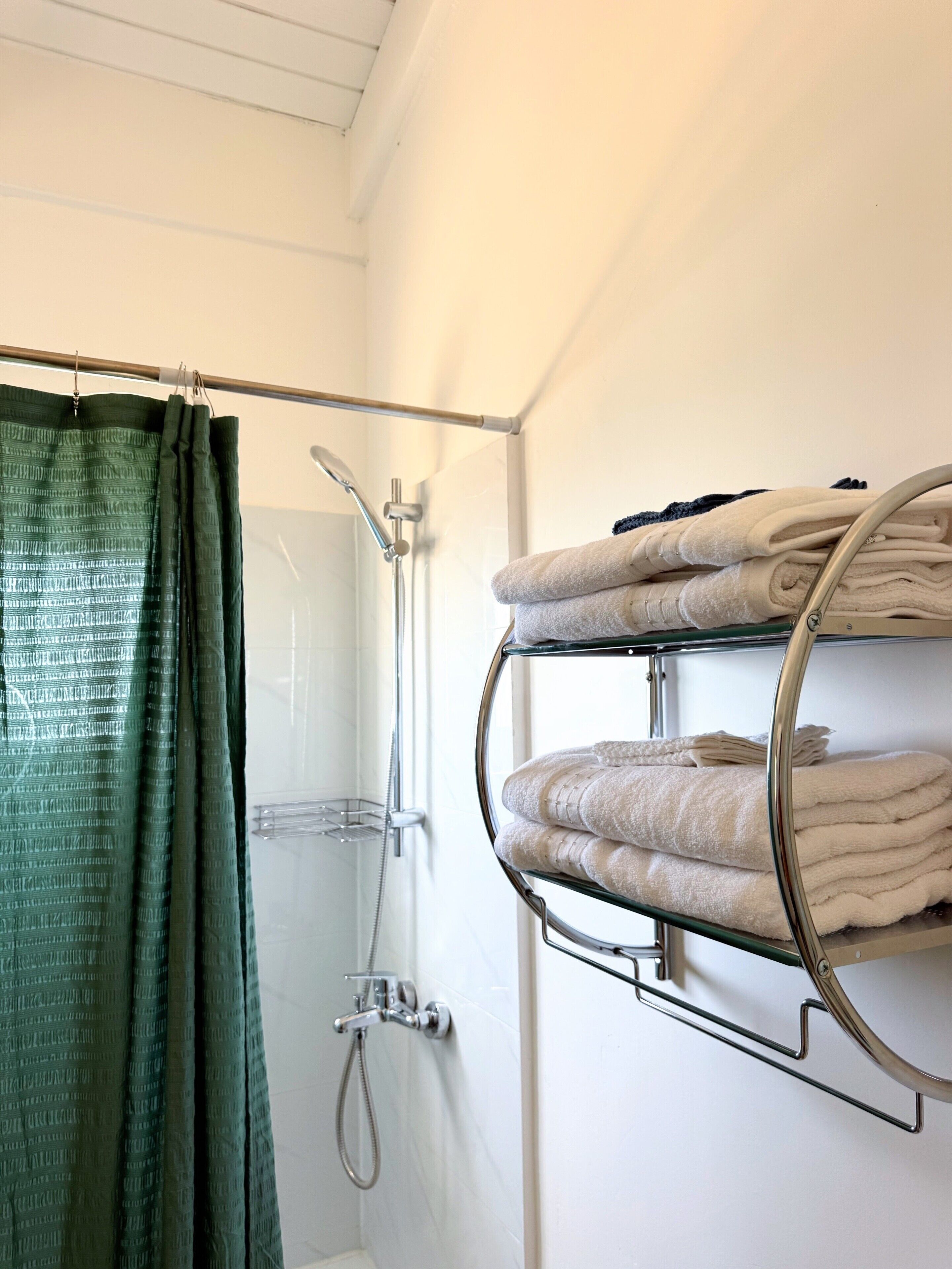 A bathroom with a shower, a towel rack with folded towels, and a green shower curtain.