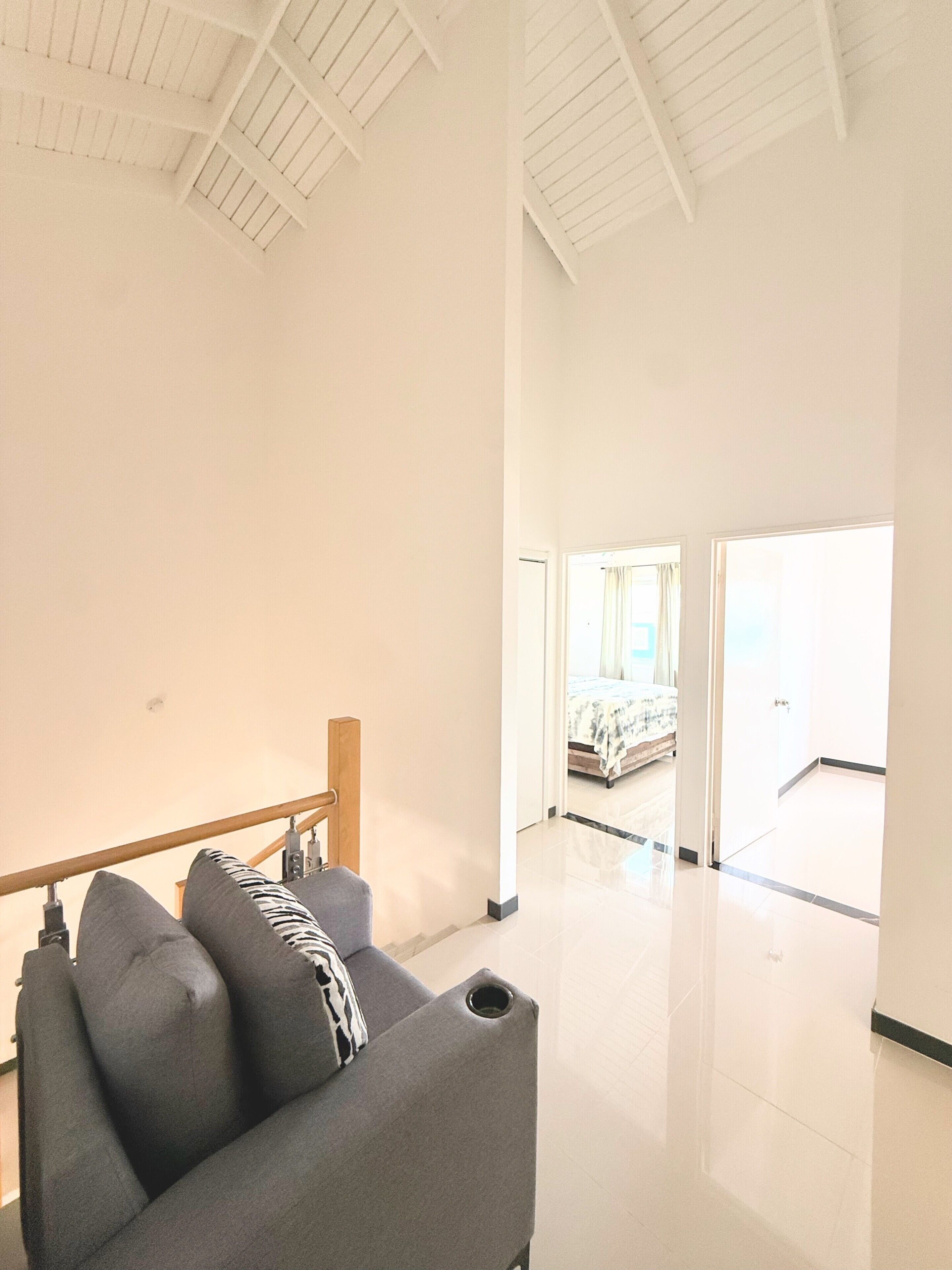 A spacious room with a high ceiling, a bed in the background, and a seating area with a bench and cushions.